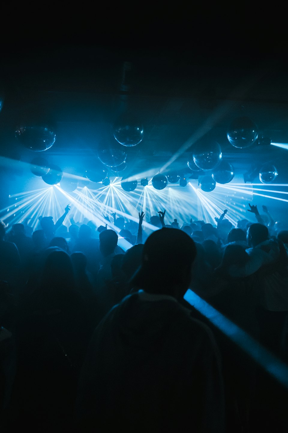 Menschenmenge mit erhobenen Händen bei einem blau beleuchteten Konzert mit Discokugeln.