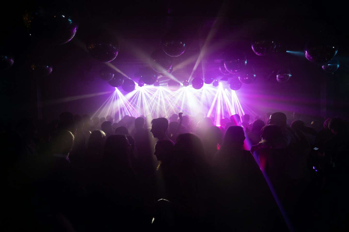 Menschen tanzen unter leuchtenden Laserlichtern und Discokugeln.