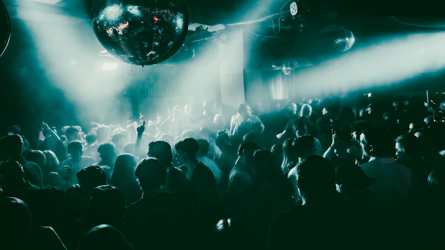 Menschen tanzen unter Discokugeln in einem vollen Nachtclub.