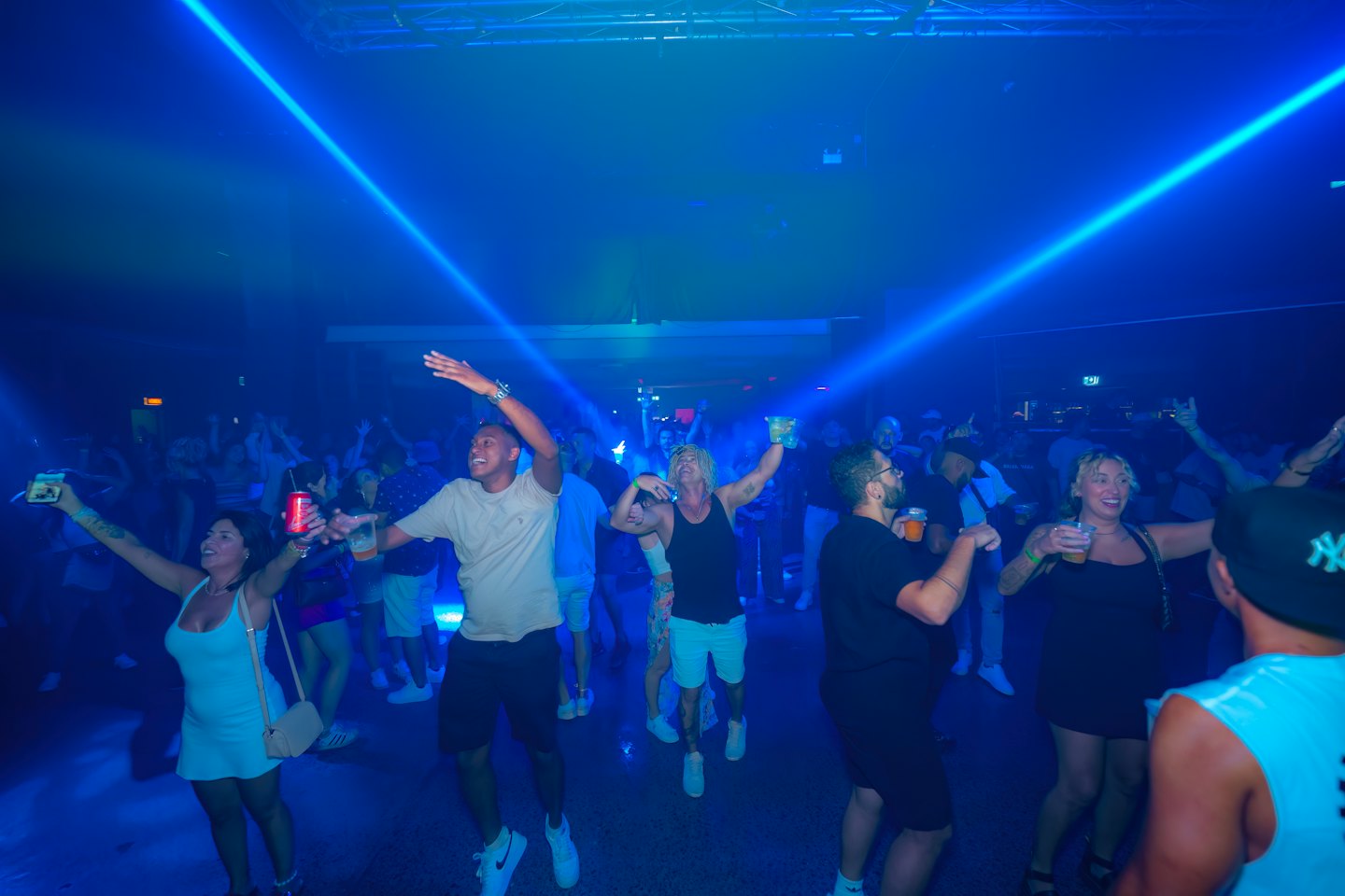 Vielfältige Gruppe von Menschen, die in einem Nachtclub bei blauen Lichtern energisch tanzen.